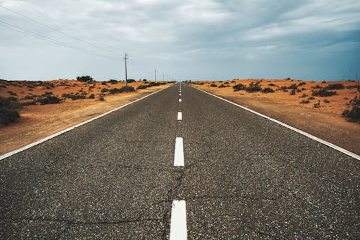 Straight, empty desert road under cloudy sky in Dubai, UAE, highlighting solitude and vastness.