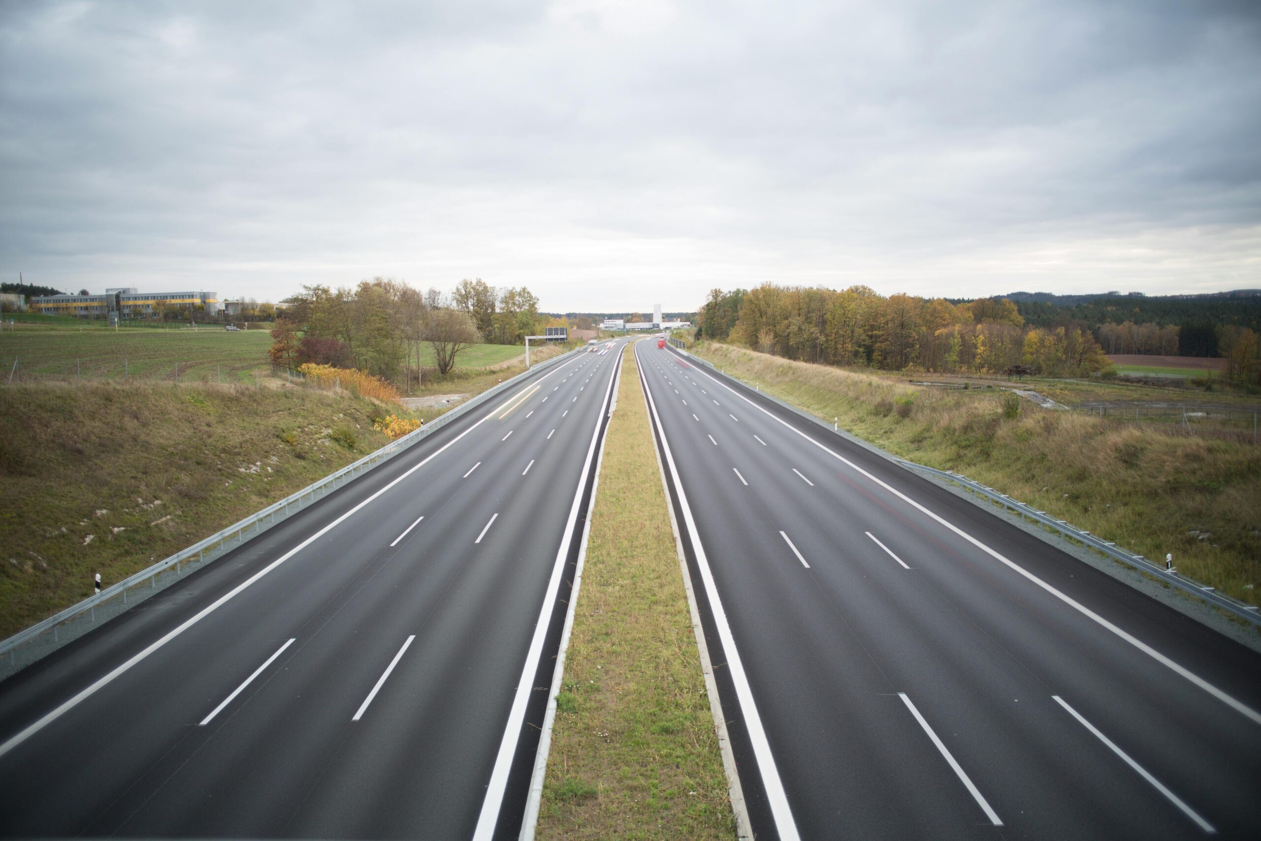 A serene image of an empty highway stretching through a peaceful countryside under a cloudy sky.
